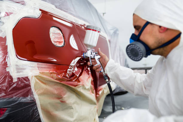 Man with protective clothes and mask painting car using spray compressor.